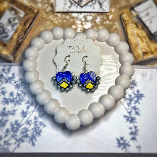 Handmade heart earrings in blue with yellow accents displayed on a white beaded heart-shaped tray