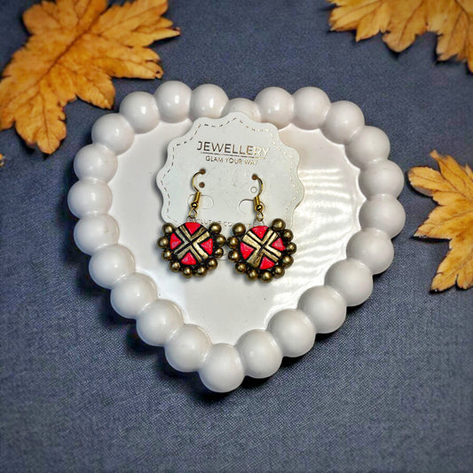 Bohemian handcrafted earrings with red and gold design displayed on white heart-shaped dish