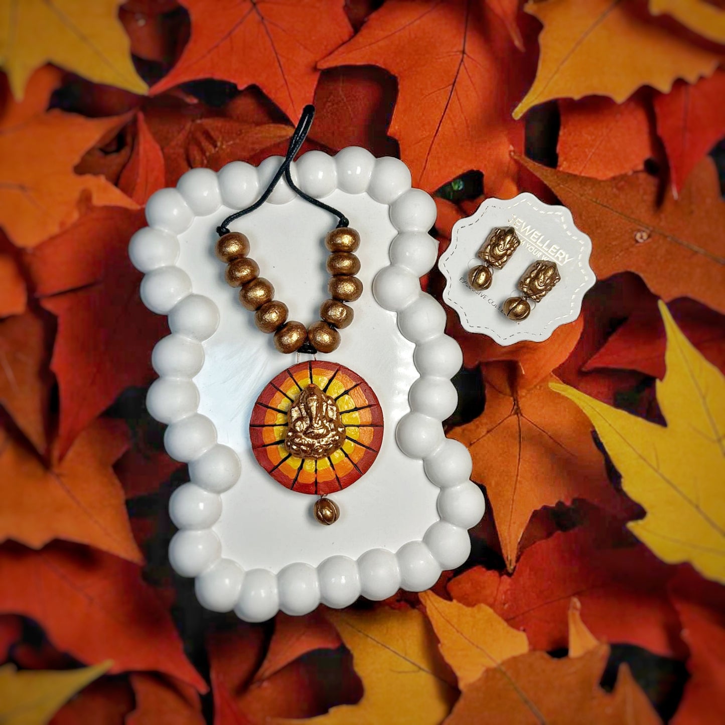Handmade Ganesha necklace with golden beads and pendant displayed on white tray with matching earrings 