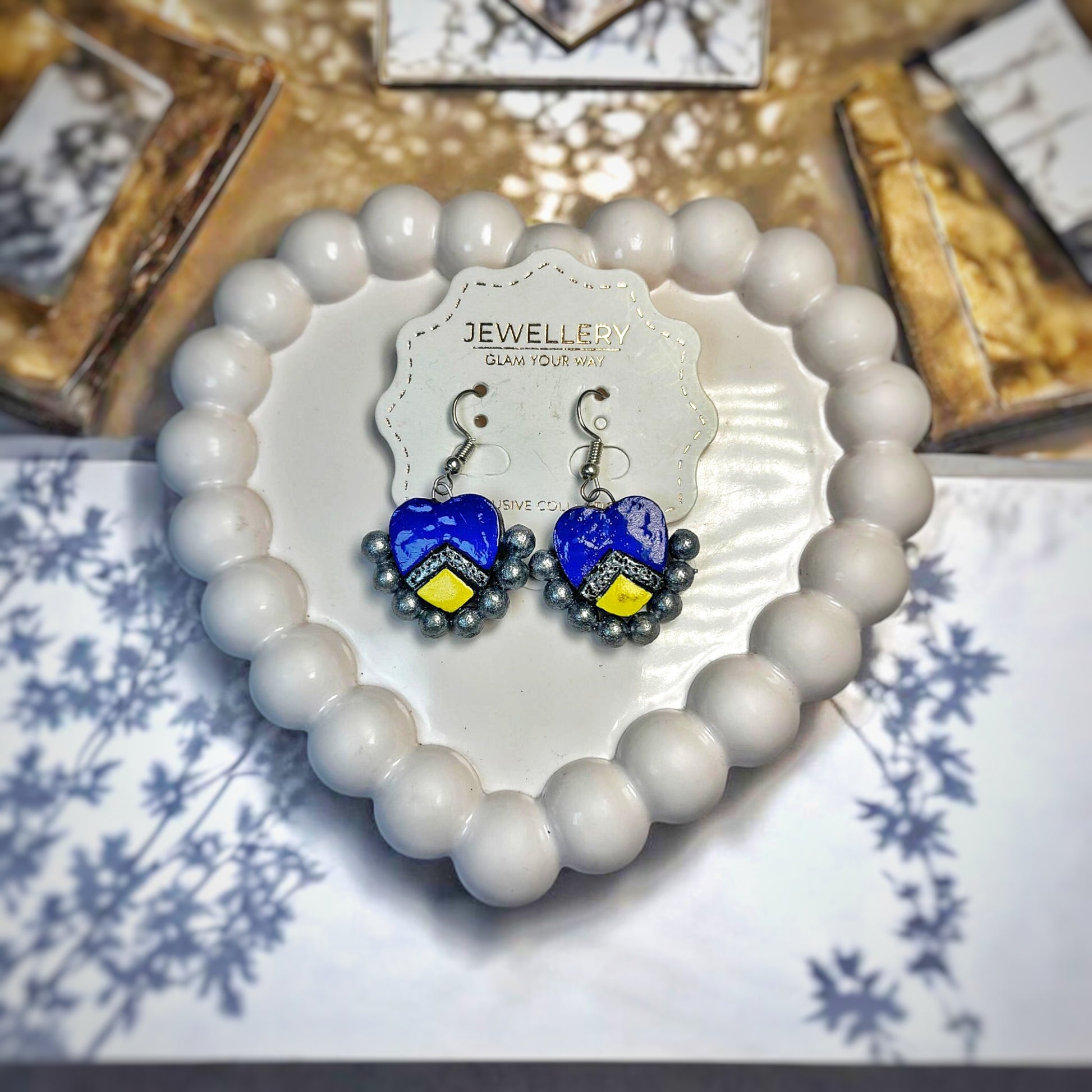Handmade heart earrings in blue with yellow accents displayed on a white beaded heart-shaped tray