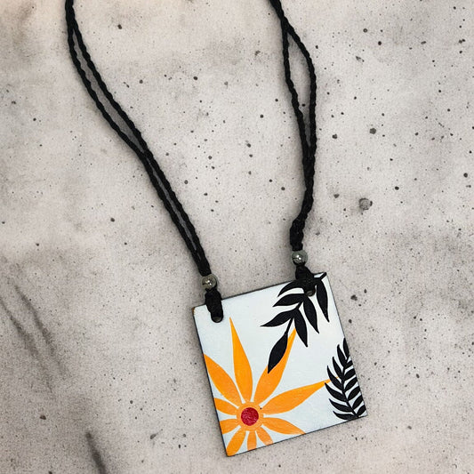 Handmade necklace for women with black braided cord and square pendant featuring orange flower and black leaves design