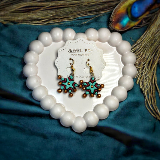 Handmade star earrings with turquoise and brown beads displayed on a white heart-shaped plate