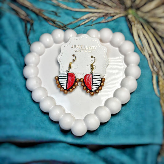 Handmade terracotta earrings in red white and brown beads displayed on a heart shaped white ceramic tray