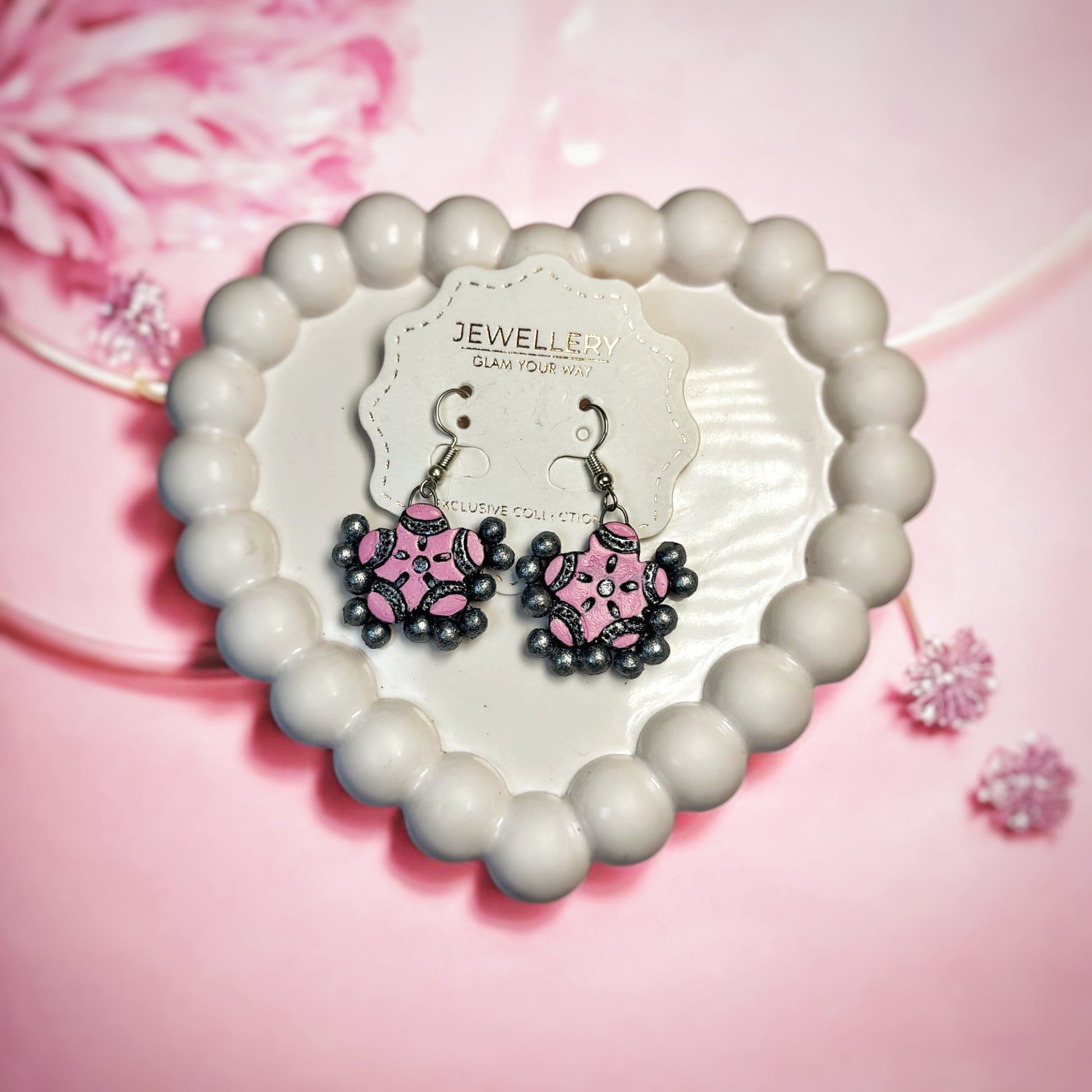 Traditional pink drop earrings with black bead accents displayed on a heart-shaped white tray